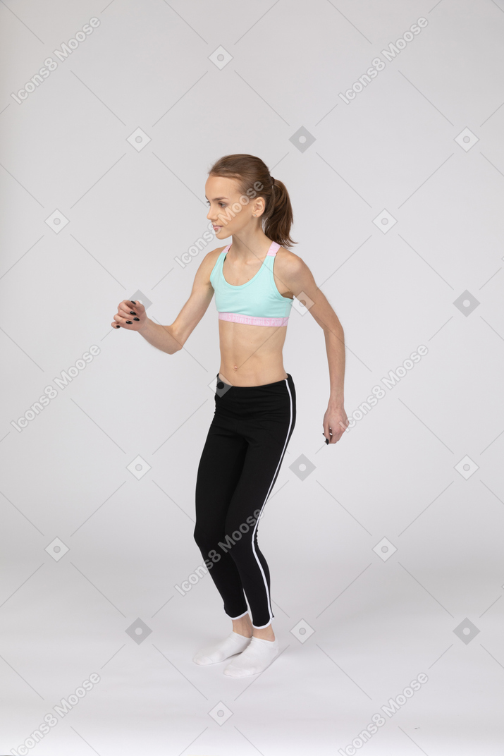 Three-quarter view of a teen girl in sportswear bending knees and raising hand