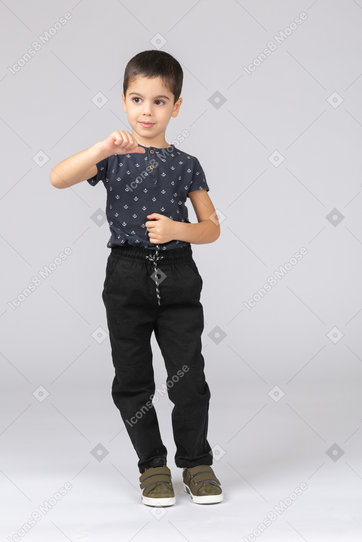 Вид спереди симпатичного мальчика в повседневной одежде, показывающего большой палец вниз