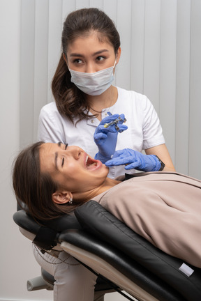 Um dentista sério tentando fazer uma injeção em sua paciente gritando