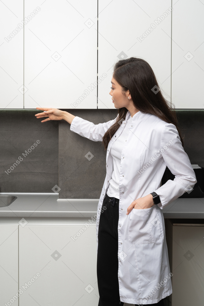 Vista de tres cuartos de una joven doctora observando su gabinete médico
