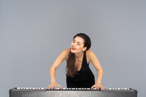 Front view of a smiling young lady in black dress leaning on the piano