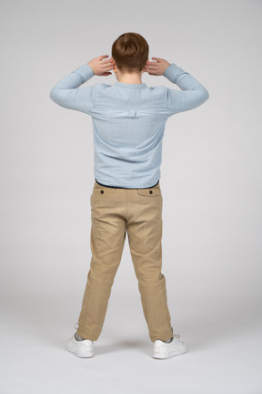 Back view of a boy standing with hands on head