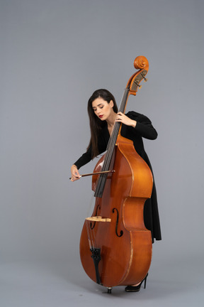 Three-quarter view of a young woman in black dress playing the double-bass with a bow