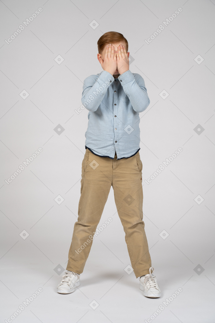 Vista frontal de un niño que cubre la cara con las manos