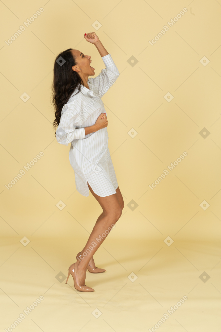 Vista lateral de una mujer joven de piel oscura bailando en su vestido blanco levantando las manos