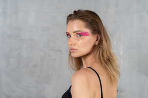 Young woman with bright pink eye make-up looking over her shoulder