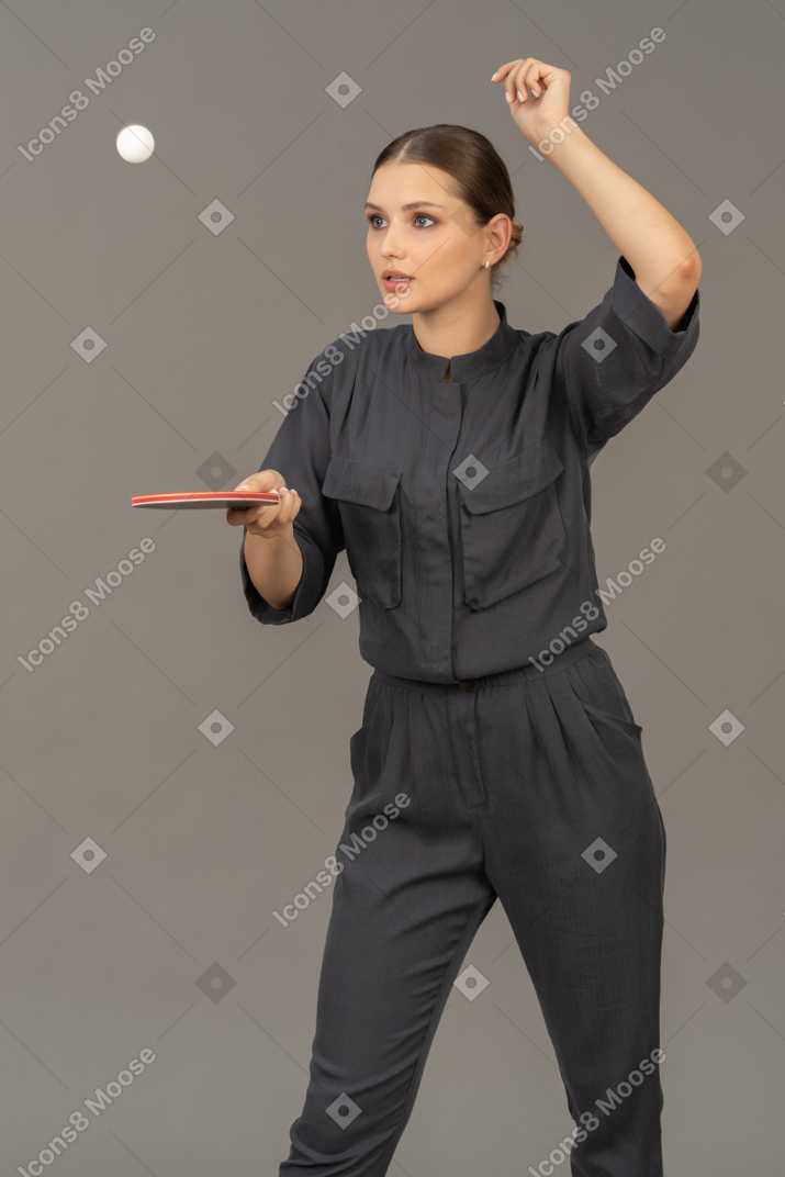 Three-quarter view of young woman in a jumpsuit playing table tennis