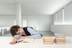 A boy sleeping on top of a table next to a stack of books