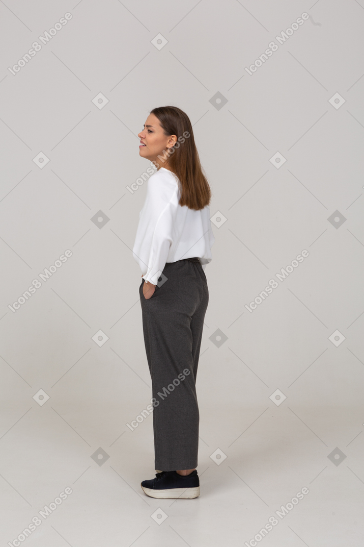 Три четверти сзади уставшей молодой леди в офисной одежде, засовывающей руки в карманы