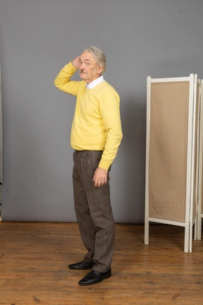 Three-quarter view of an old man in a yellow pullover touching his head
