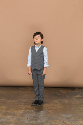 Front view of a seirous boy in grey suit standing still
