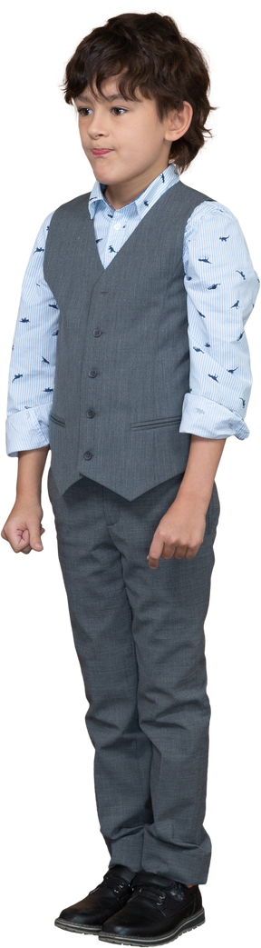 Vista frontal de un niño en traje parado y haciendo muecas