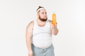 Um homem gordo triste no sportswear segurando uma garrafa de suco