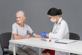 Femme aînée détourne le regard tandis que le médecin fait son injection