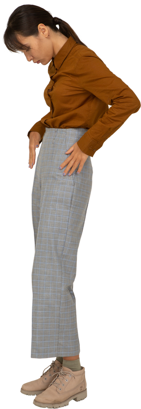 Vista laterale di una giovane donna asiatica in calzoni e camicetta che mette le mani in tasca