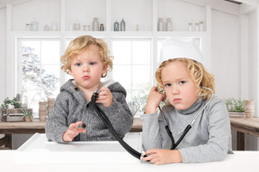 Two children sitting at a table with a stethoscope
