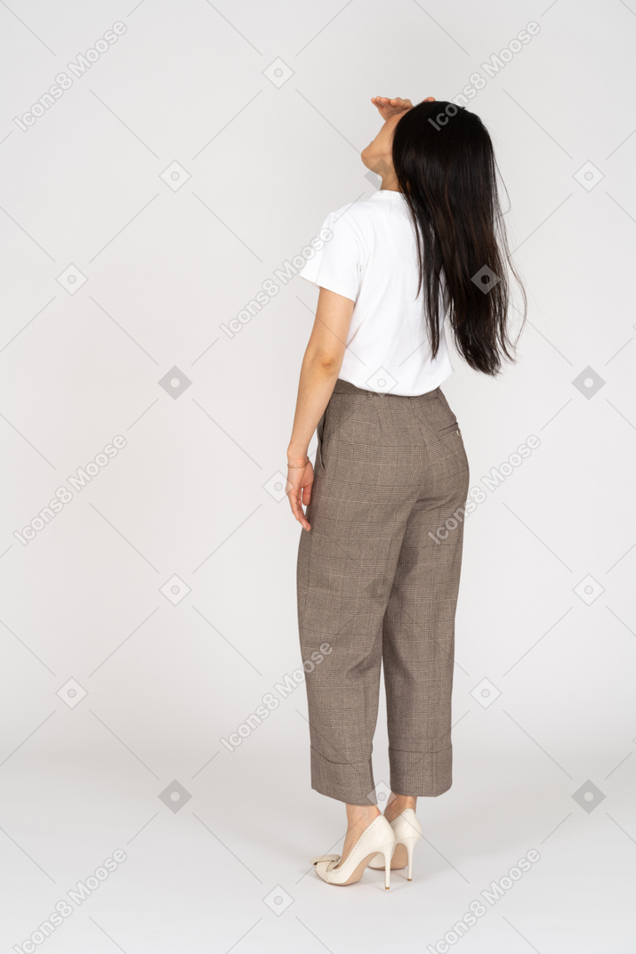 Vista posteriore di tre quarti di una giovane donna in calzoni e t-shirt alzando la mano mentre guarda in alto