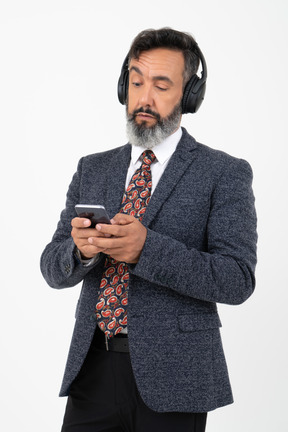 Hombre en auriculares de pie y viendo algo en su teléfono.