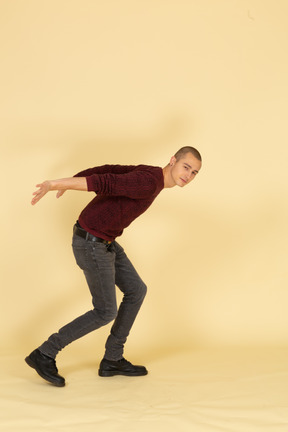 Side view of a young man in red pullover standing while taking hands behind