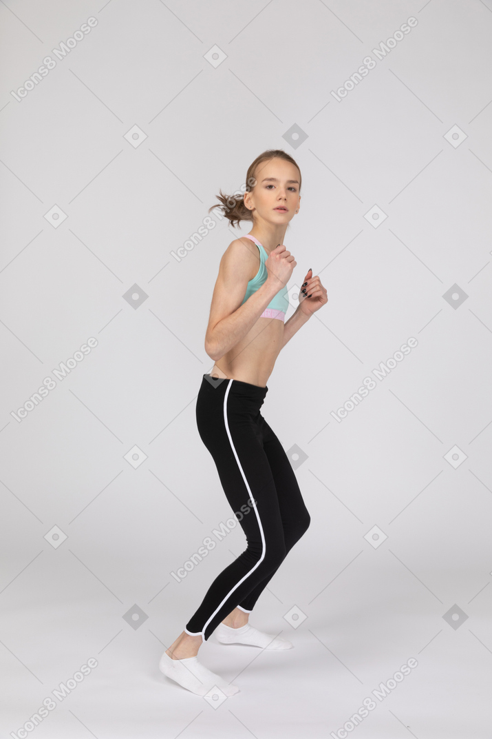 Vista frontal de uma adolescente em roupas esportivas agachada enquanto fecha os punhos