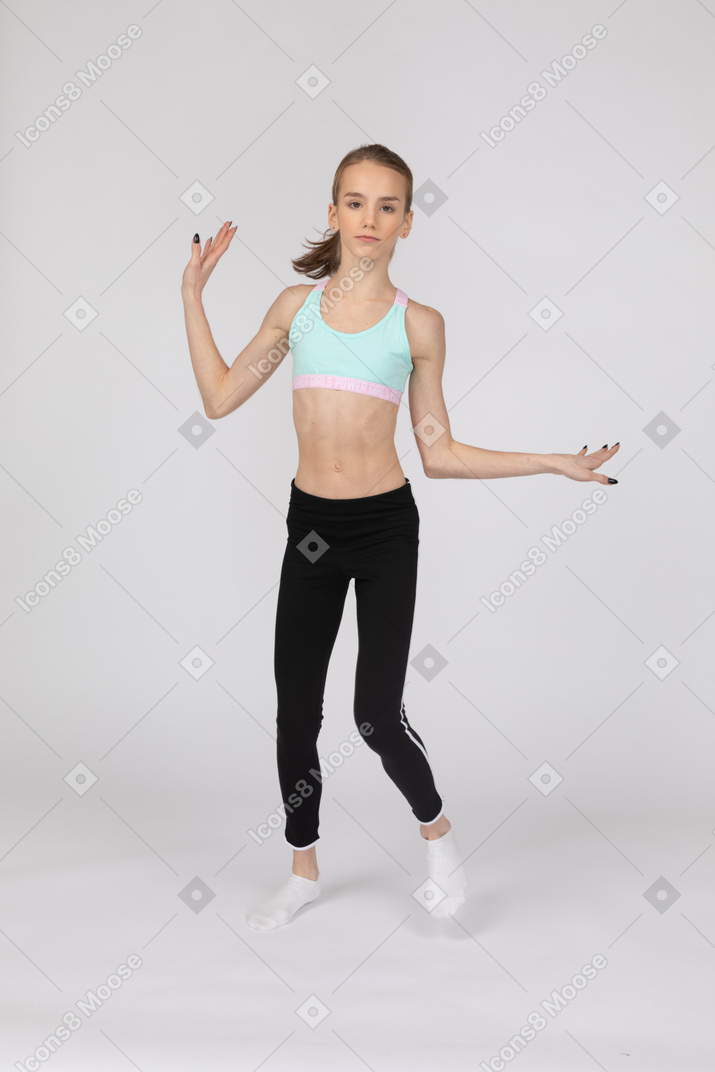 Vista frontal de uma adolescente em roupas esportivas, levantando as mãos e dançando