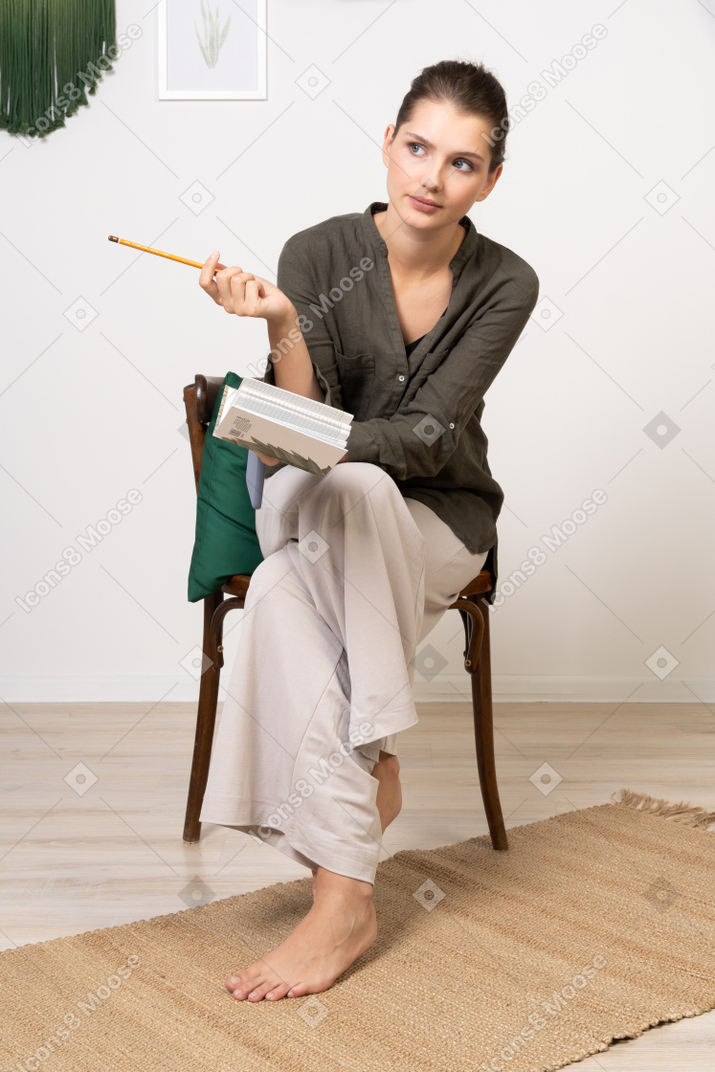 Vue de face d'une jeune femme réfléchie portant des vêtements de maison assise sur une chaise avec un crayon et un ordinateur portable