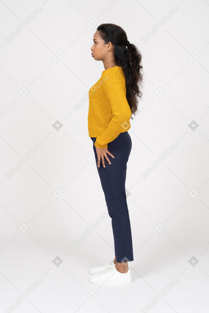 Vista lateral de uma garota com roupas casuais em pé com a mão no quadril