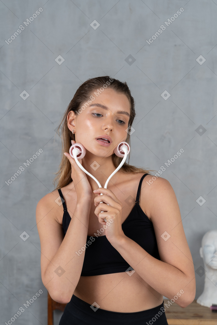 Jolie jeune femme massant son visage avec un rouleau facial