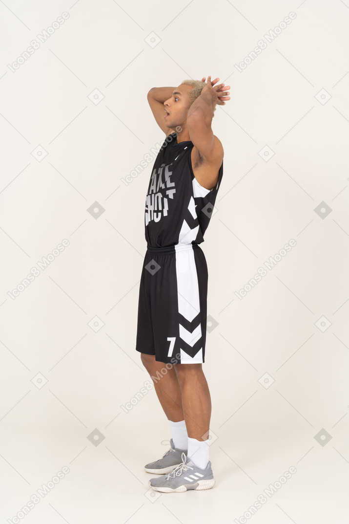Vista lateral de un joven jugador de baloncesto masculino sorprendido tocando la cabeza