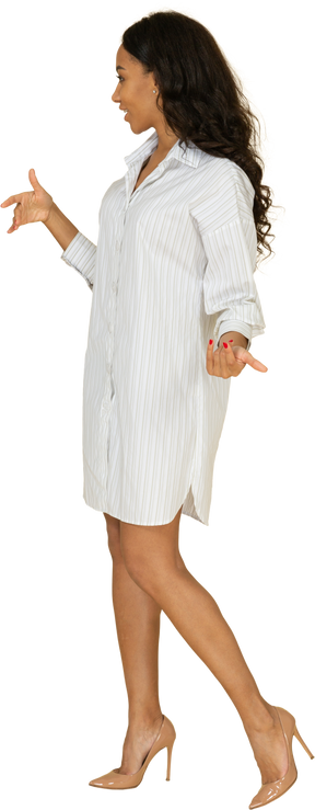 Вид в три четверти вопрошающей жестикулирующей темнокожей молодой женщины в белом платье