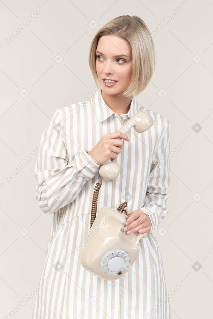Mujer joven distraída con teléfono rotatorio antiguo