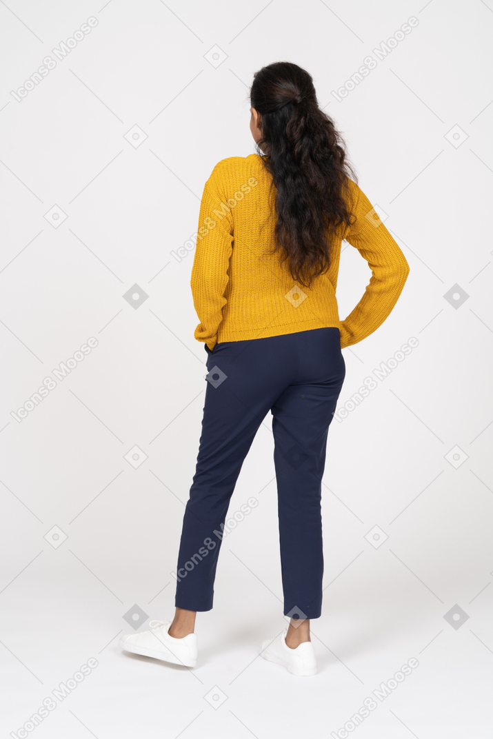 Вид сзади девушки в повседневной одежде, позирующей с руками в карманах