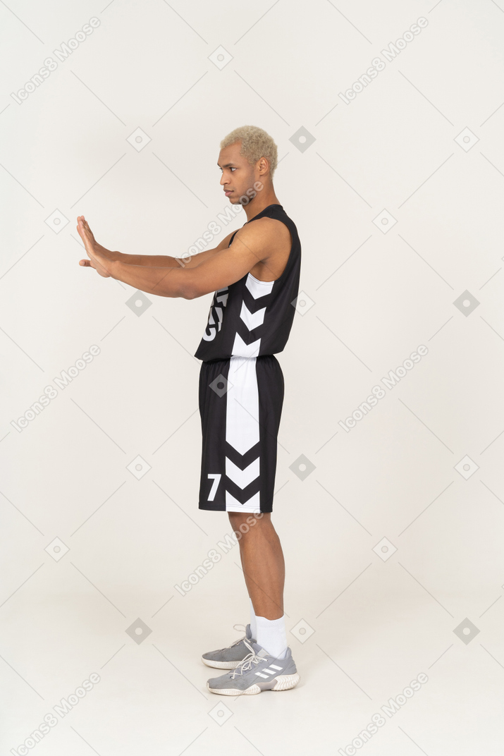 Vista lateral de un joven jugador de baloncesto masculino que se niega extendiendo sus brazos