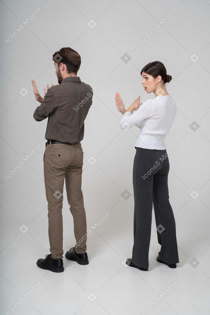 Vista traseira de três quartos de um jovem casal com roupas de escritório, cruzando os braços