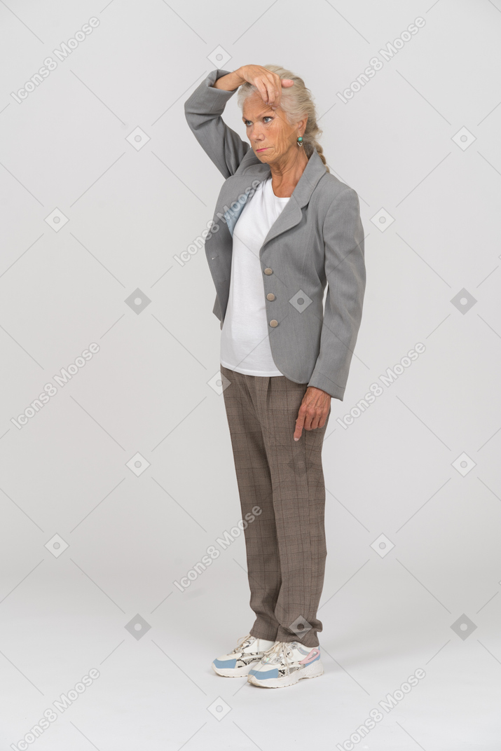 Front view of an old woman in suit touching forehead