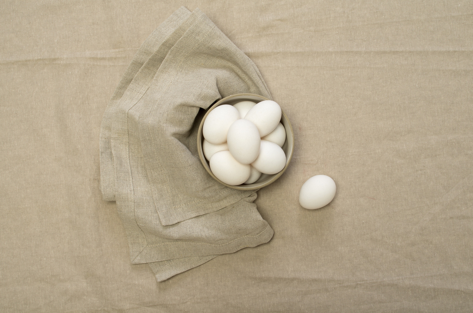White chicken eggs in a bowl, grey tablecloth and a dish-cloth