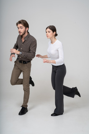 Vue de trois quarts d'un jeune couple en tenue de bureau levant la jambe