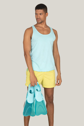 A man in yellow shorts and a blue tank top holding swimfins