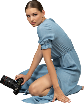 Vue latérale d'une jeune femme en robe bleue assise sur un sol avec appareil photo
