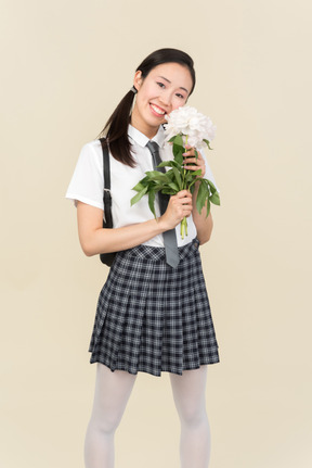 Улыбающаяся азиатская школьница с цветами в руках