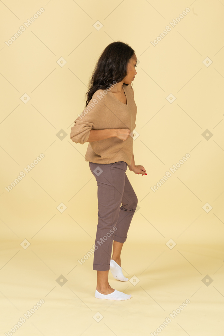 Three-quarter back view of a dancing dark-skinned young female bending knee