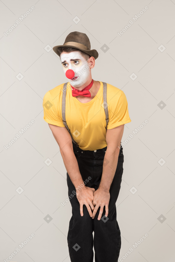 Sad male clown standing with hands behind the back