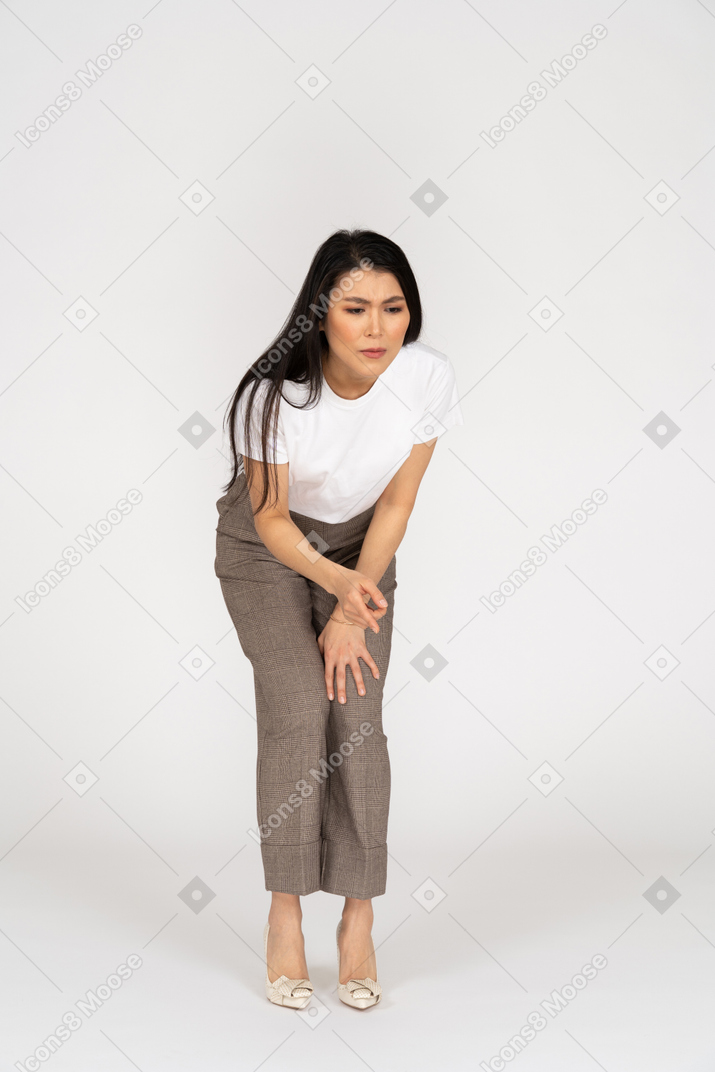 Front view of a perplexed young lady in breeches and t-shirt bending down