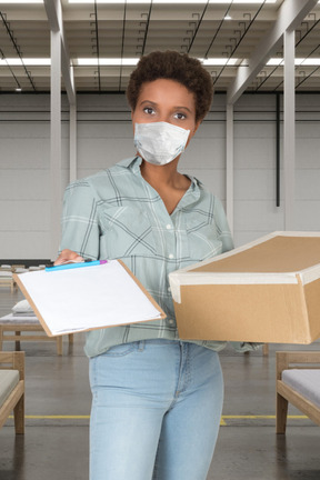 A woman wearing a face mask and holding a box