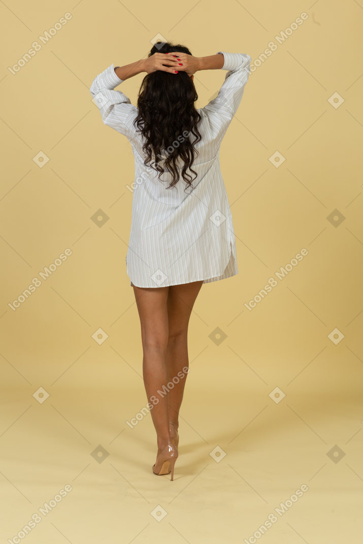 ポニーテールを作る白いドレスを着た浅黒い肌の若い女性の背面図