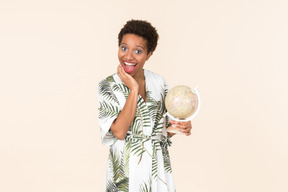 Black short-haired woman in a white and green dress, standing with a globe in her hand