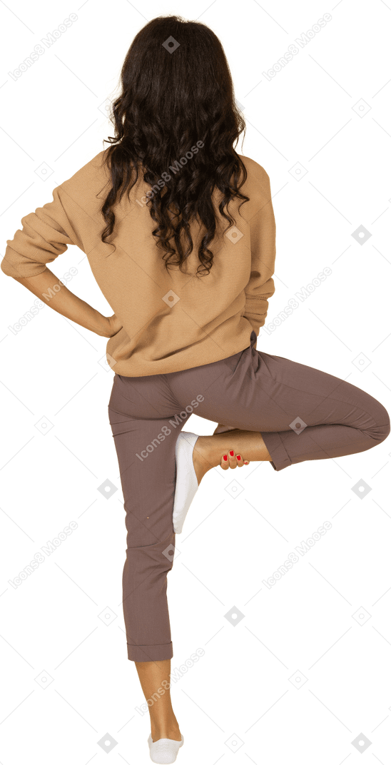 Vista traseira de uma jovem mulher de pele escura colocando a mão no quadril enquanto levanta a perna