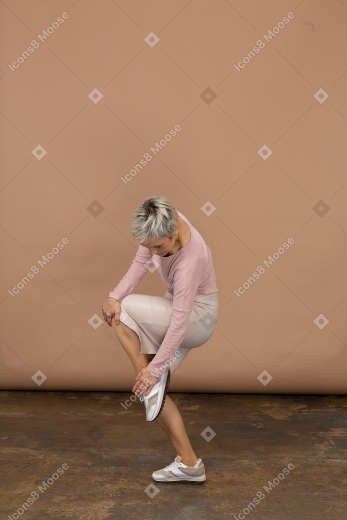 Vista lateral de uma mulher com roupas casuais, apoiada em uma perna e tocando seu sapato