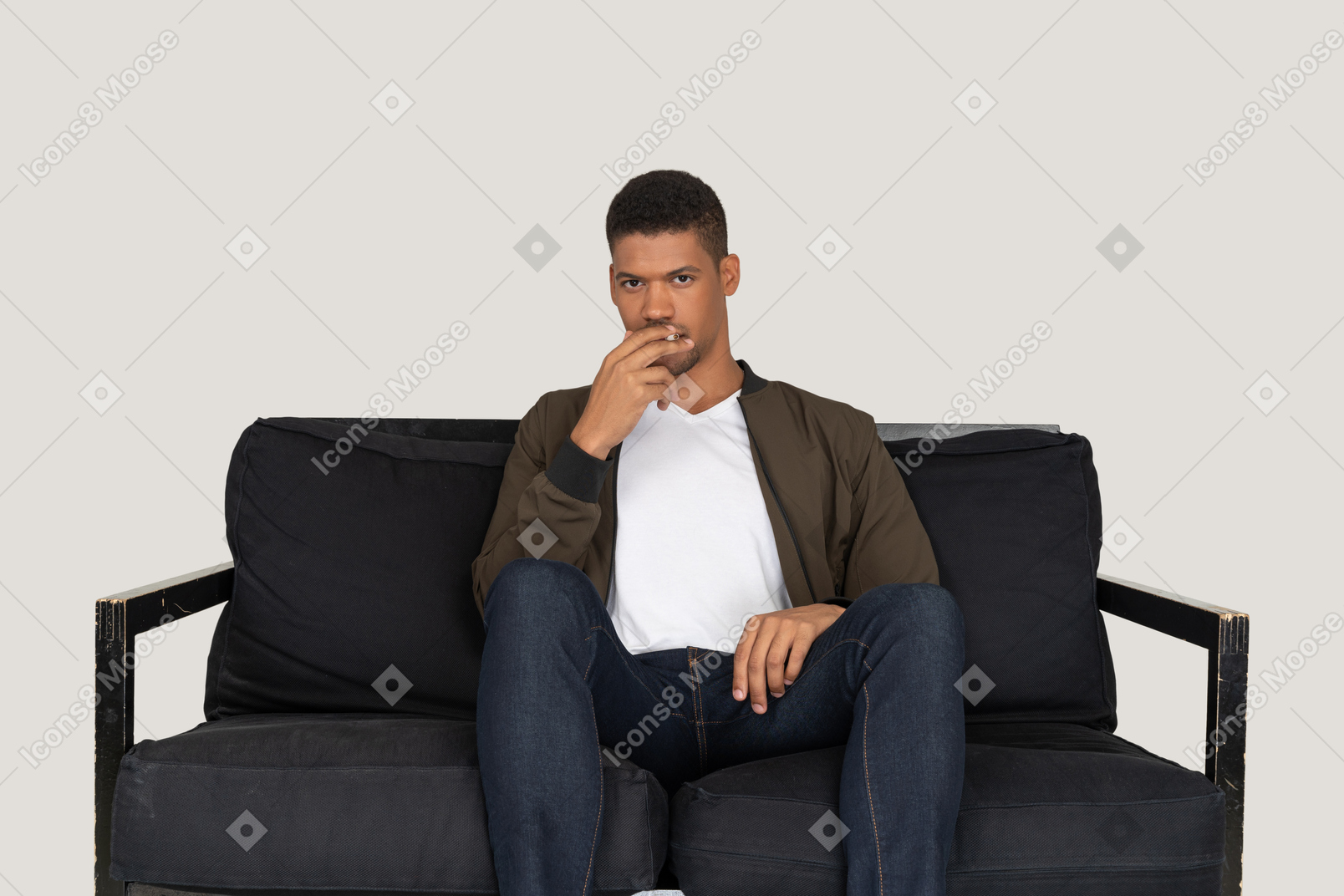 Vista frontal de um jovem sentado em um sofá segurando um cigarro na boca