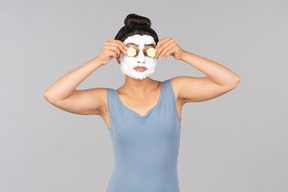 Donna con maschera facciale bianca applicando fette di cetriolo sugli occhi